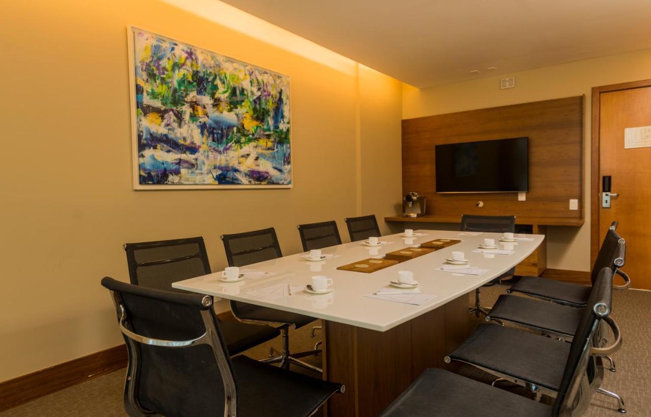 Hotel Luzeiros Sao Luis Экстерьер фото The photo shows a modern conference room. It features a long rectangular table surrounded by eight black chairs. On the table, there are several small white cups and a decorative runner. The room is illuminated with soft lighting, and there is a larg